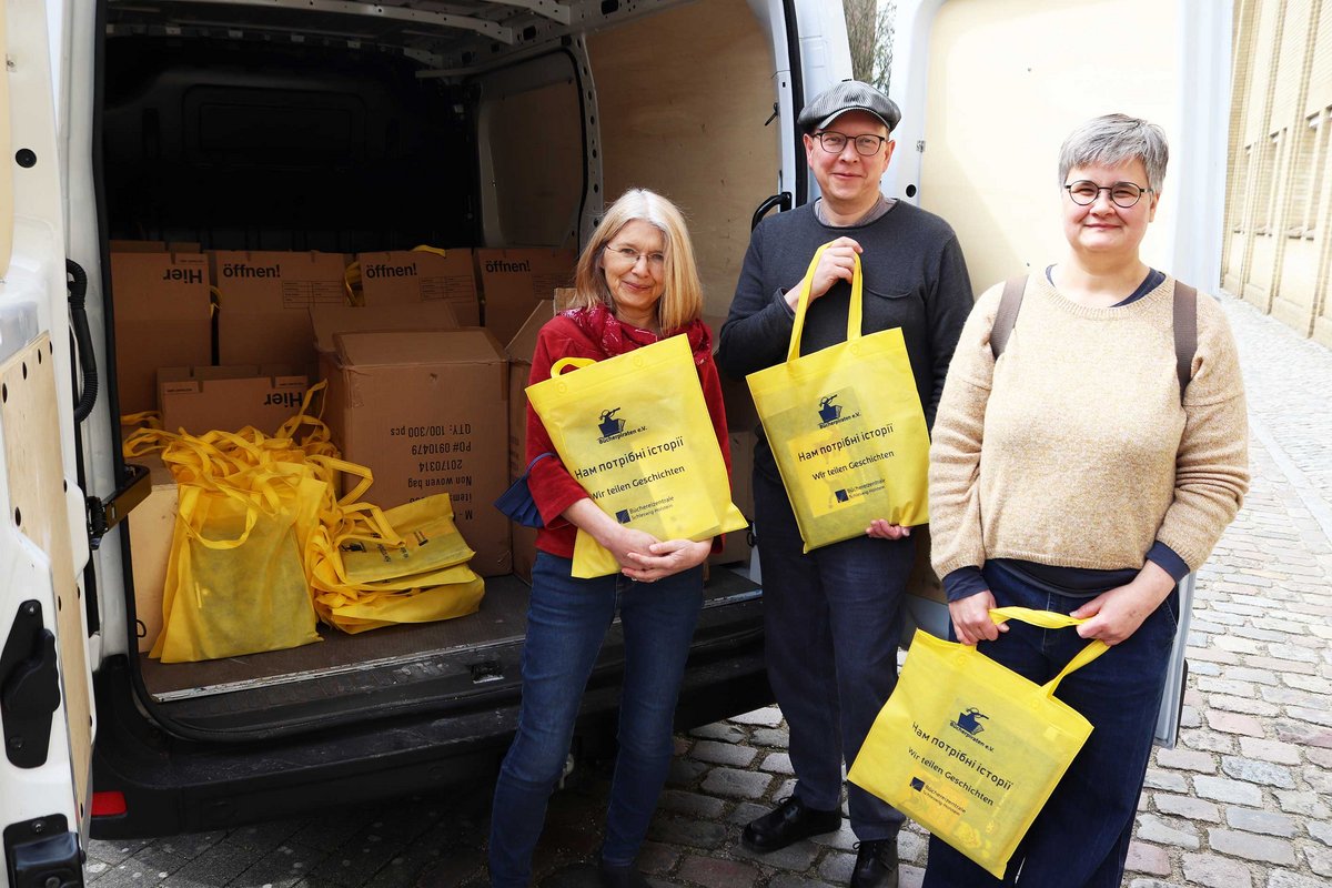 Projektleiterin Susanne Brandt (Büchereizentrale Schleswig-Holstein), Martin Gries und Lenara Sanders (beide Lübecker Bücherpiraten, von links nach rechts) stehen vor einem Kleinbus mit den ersten 500 gepackten Büchertaschen für Geflüchtete aus der Ukraine. 