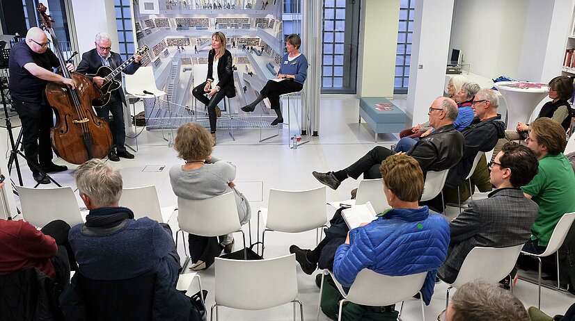 Gesprächspartner, Musiker und das Publikum im offenen Bibliotheksraum beim MusikGespräch: Veranstaltung mit Gabriele Zerweck, der zweiten Geschäftsführerin der Ludwigsburger Schlossfestspiele (hinten, Zweite von rechts) im April 2023. Foto: Diana Balser-Steck