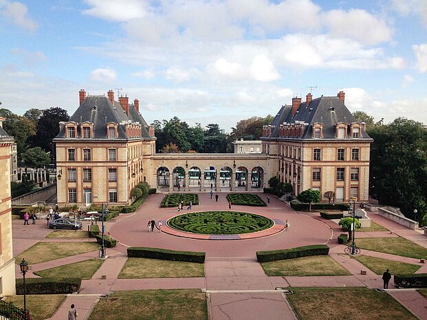 Das Foto zeigt den Eingang zum Campus der Cité Internationale Universitaire. Die Studierenden kommen durch sieben Rundbögen, an die links und rechts ein Gebäude grenzt auf den Campus.