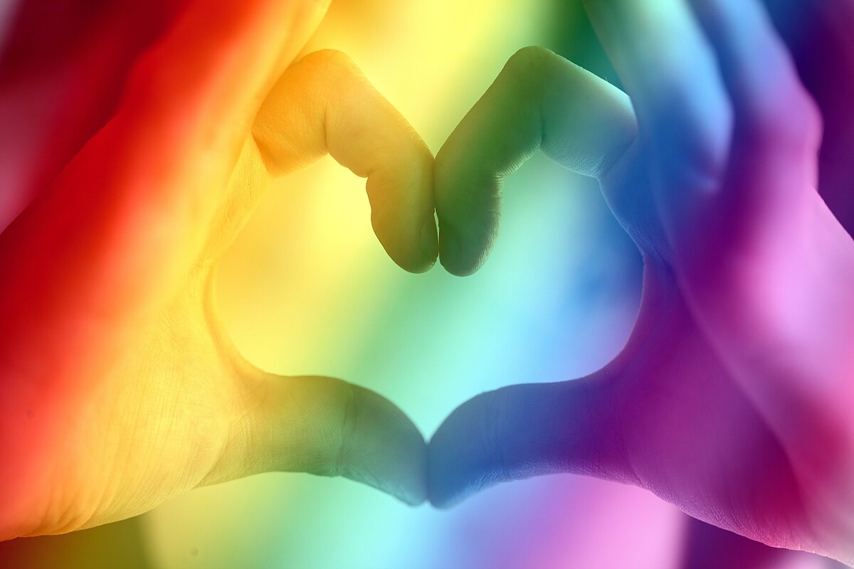 Alle Menschen sind gleich: Ein mit den Fingern angedeutetes Herz mit Regenbogenfarben darüber.